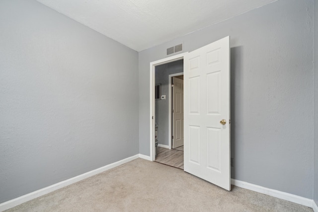 unfurnished bedroom with light carpet, baseboards, visible vents, and a textured wall