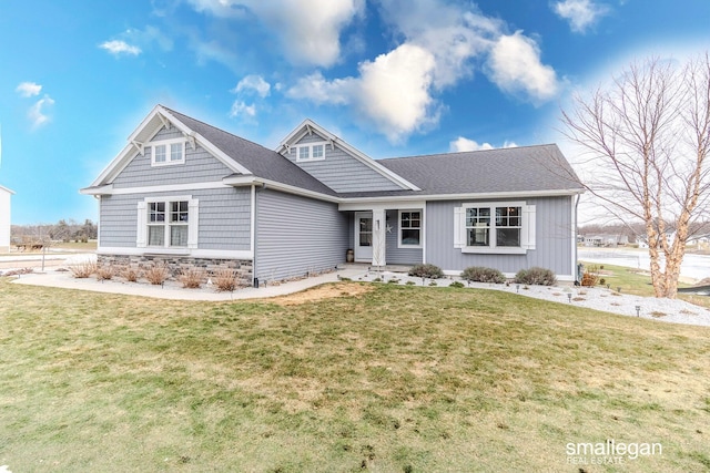 view of front of home featuring stone siding, a front lawn, and roof with shingles