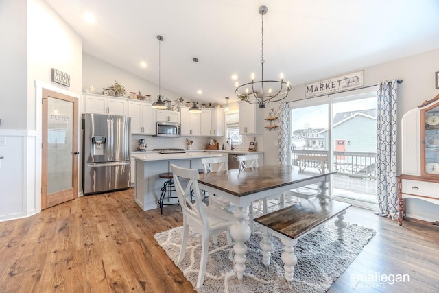 dining area with high vaulted ceiling, light wood finished floors, and an inviting chandelier