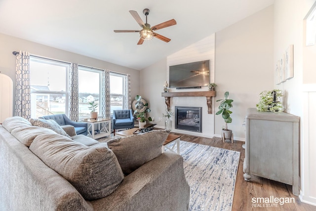 living area featuring a fireplace, a ceiling fan, wood finished floors, high vaulted ceiling, and baseboards