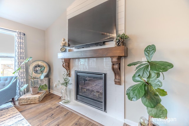 interior space with a tiled fireplace, wood finished floors, and baseboards