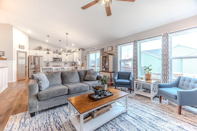 living room featuring lofted ceiling, light wood finished floors, and ceiling fan with notable chandelier