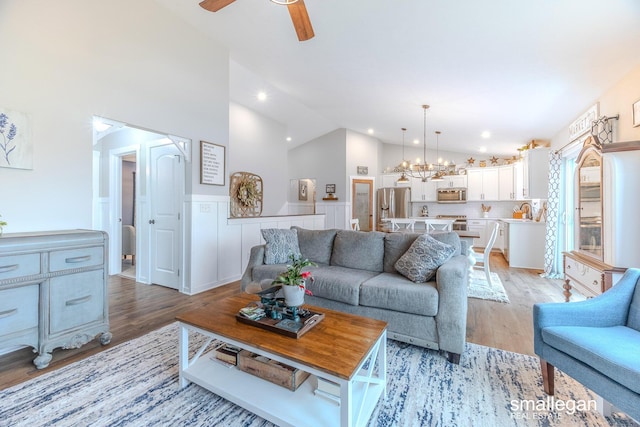 living area with wainscoting, ceiling fan with notable chandelier, light wood-type flooring, high vaulted ceiling, and recessed lighting