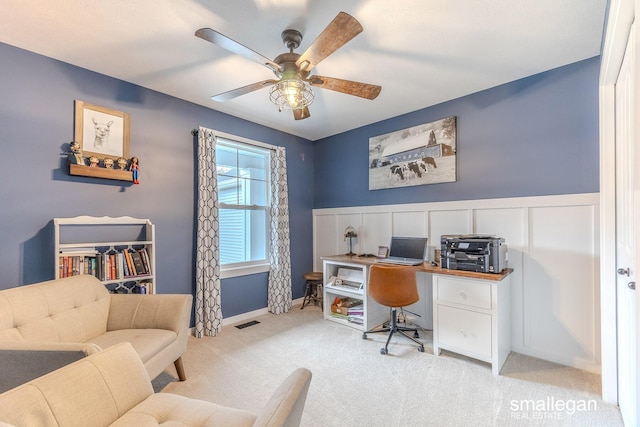 office area with ceiling fan, a decorative wall, a wainscoted wall, light colored carpet, and visible vents