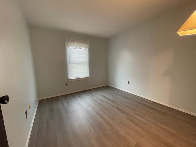 spare room featuring wood finished floors, visible vents, and baseboards