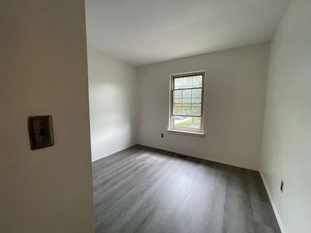 empty room with wood finished floors, visible vents, and baseboards