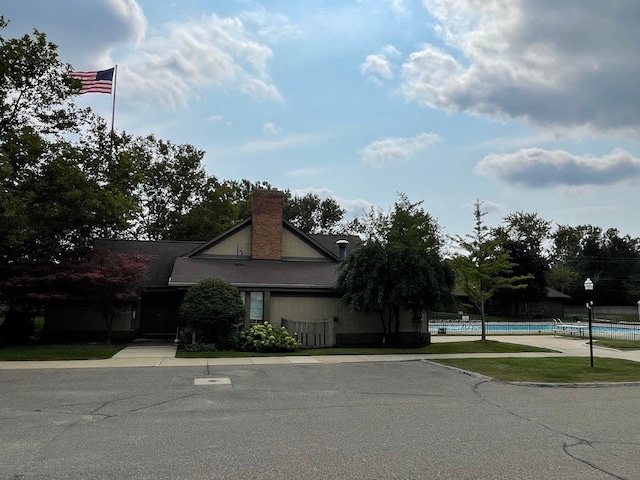 view of front facade featuring an outdoor pool, a chimney, and fence