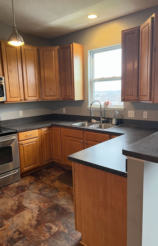 kitchen featuring dark countertops, hanging light fixtures, a sink, range, and a peninsula