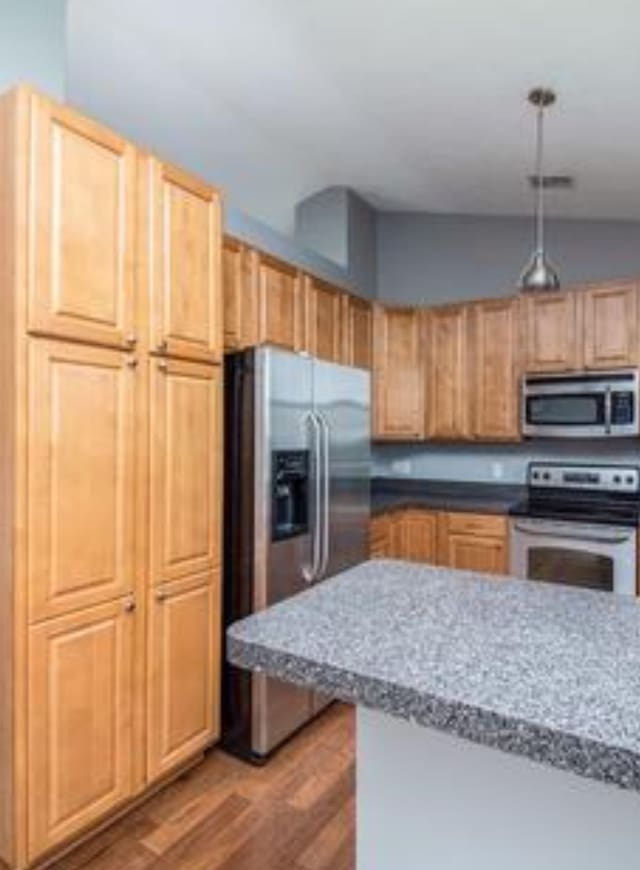 kitchen featuring light wood finished floors, appliances with stainless steel finishes, decorative light fixtures, and light brown cabinetry