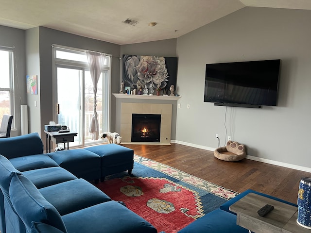 living area with visible vents, baseboards, a tiled fireplace, lofted ceiling, and wood finished floors