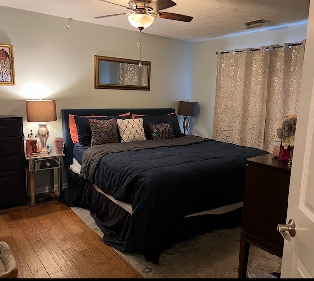 bedroom featuring a ceiling fan, a textured ceiling, visible vents, and wood finished floors