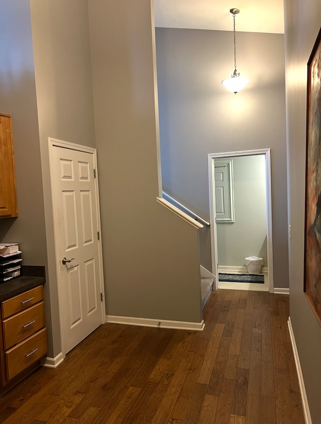 hall featuring a towering ceiling, dark wood-style floors, stairs, and baseboards