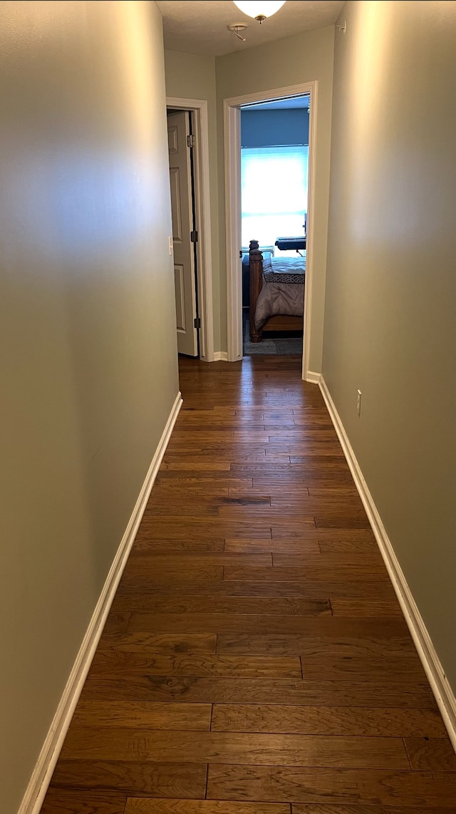 hallway featuring dark wood-style flooring and baseboards