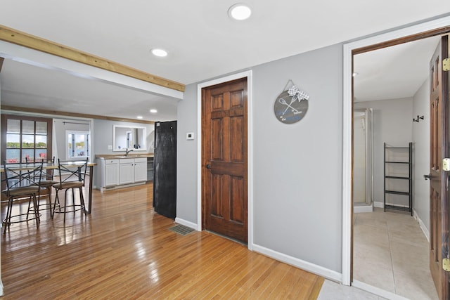 entryway with light wood-style floors, recessed lighting, beam ceiling, and baseboards