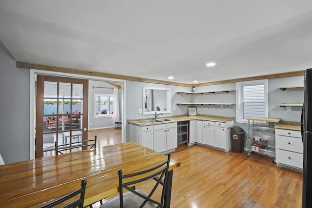 kitchen featuring light wood finished floors, open shelves, light countertops, white cabinets, and a sink