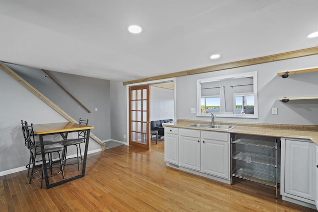 kitchen with beverage cooler, a sink, white cabinets, light countertops, and light wood finished floors