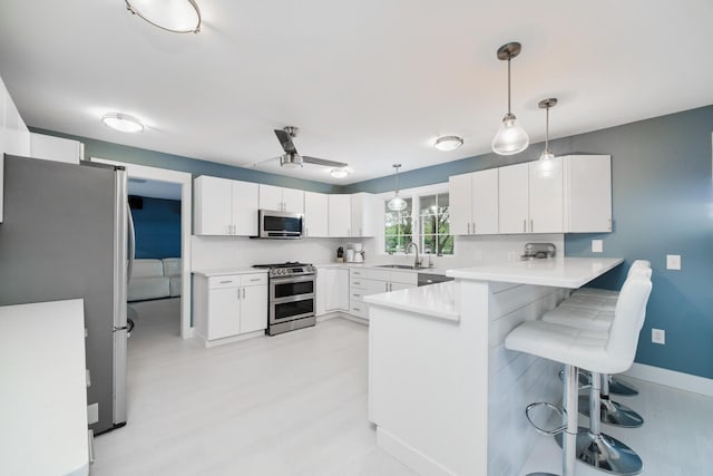 kitchen featuring a peninsula, a sink, white cabinetry, a kitchen breakfast bar, and appliances with stainless steel finishes