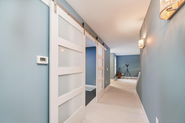 hall featuring wood finished floors, baseboards, and a barn door