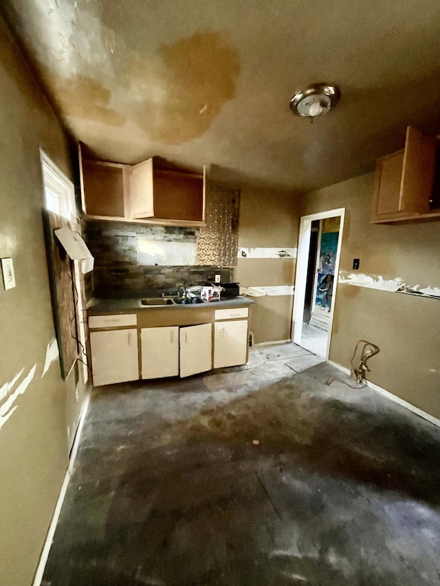 kitchen with dark countertops, backsplash, unfinished concrete flooring, and a sink