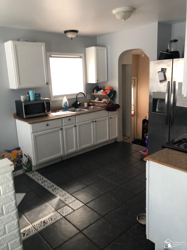 kitchen with arched walkways, a sink, white cabinets, appliances with stainless steel finishes, and dark countertops