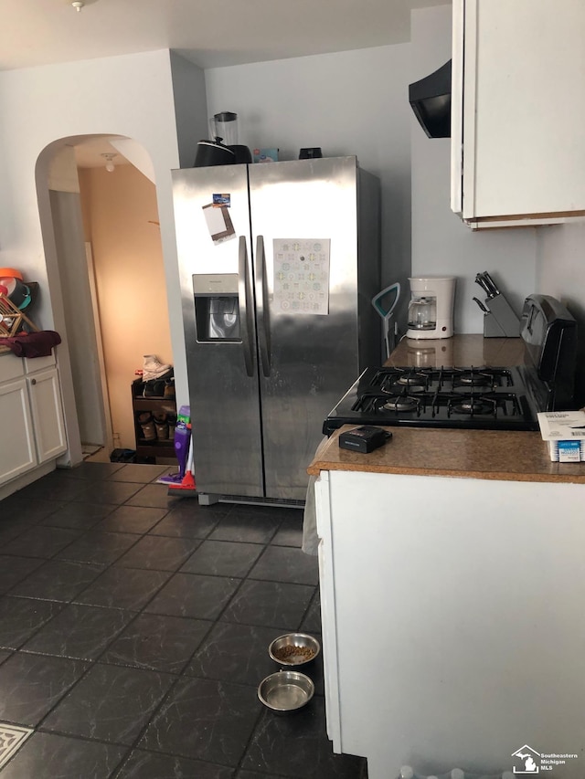 kitchen with arched walkways, dark countertops, white cabinetry, stainless steel fridge with ice dispenser, and extractor fan