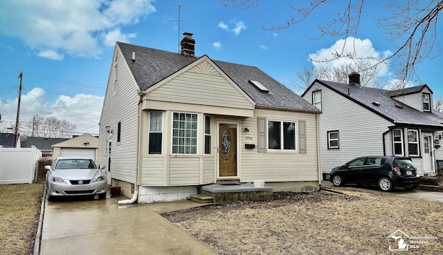 view of front of house featuring roof with shingles, a detached garage, a chimney, concrete driveway, and fence