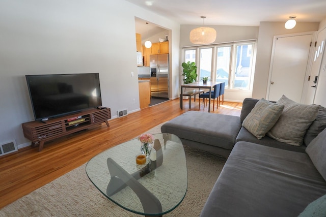 living area with vaulted ceiling, light wood finished floors, and visible vents