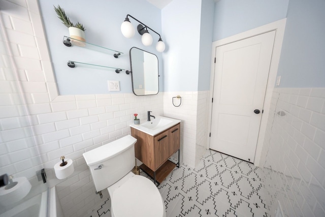 bathroom featuring toilet, wainscoting, vanity, and tile walls