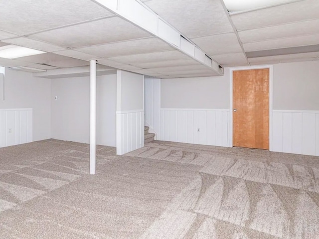 finished basement with a wainscoted wall, carpet, and a drop ceiling