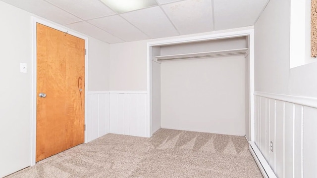 unfurnished bedroom with a drop ceiling, wainscoting, baseboard heating, carpet flooring, and a closet