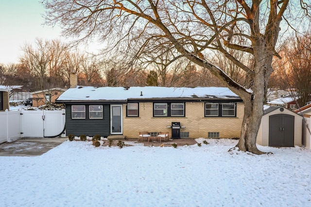 snow covered back of property featuring an outbuilding, a gate, a storage unit, fence, and brick siding