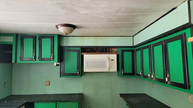 kitchen with dark countertops, green cabinetry, and white microwave