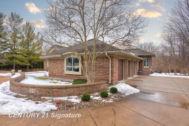 snow covered property with an attached garage, driveway, and brick siding