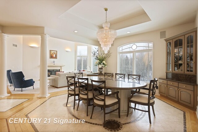 dining area featuring a chandelier, recessed lighting, a tray ceiling, a glass covered fireplace, and decorative columns