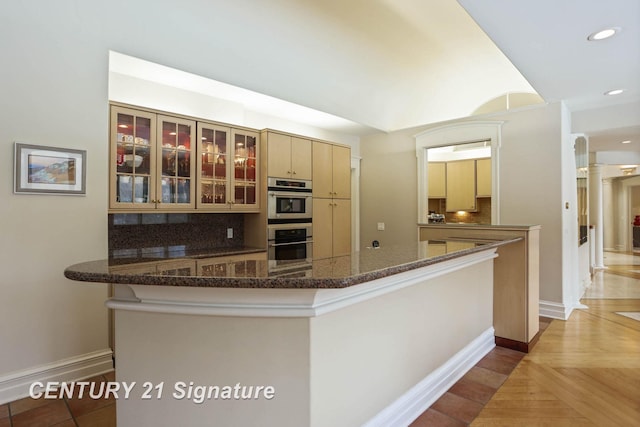 kitchen featuring dark stone counters, decorative backsplash, glass insert cabinets, double oven, and recessed lighting