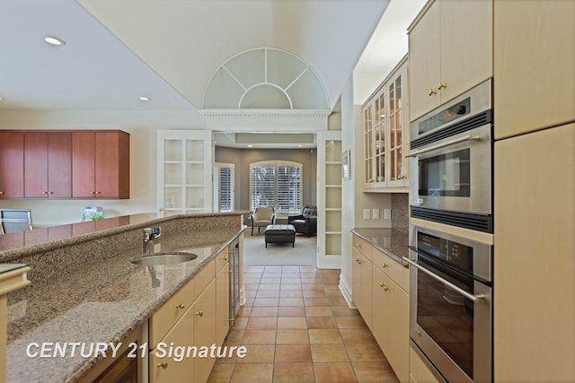 kitchen with light tile patterned floors, recessed lighting, a sink, light stone countertops, and glass insert cabinets