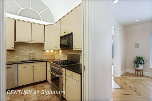 kitchen featuring stainless steel appliances, cream cabinetry, dark countertops, and a sink