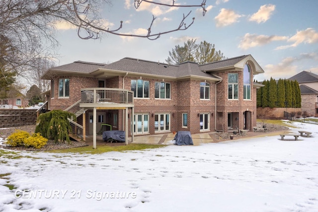 snow covered rear of property featuring brick siding, a patio, a deck, and stairs