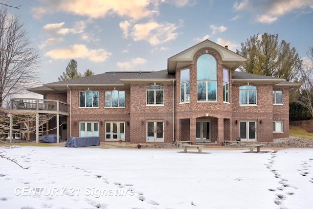 snow covered back of property featuring brick siding, a jacuzzi, and french doors