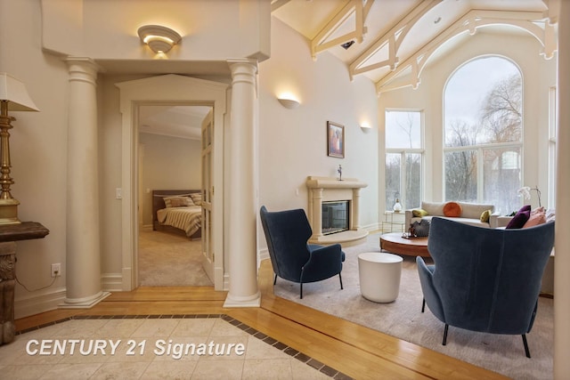 sitting room with high vaulted ceiling, wood finished floors, baseboards, a glass covered fireplace, and decorative columns