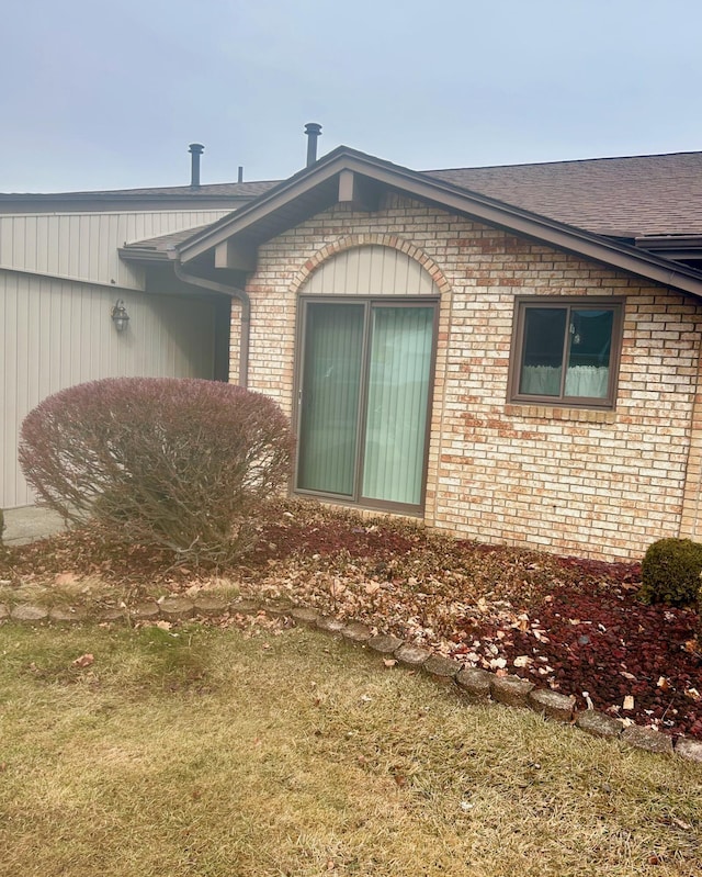 doorway to property with roof with shingles and brick siding