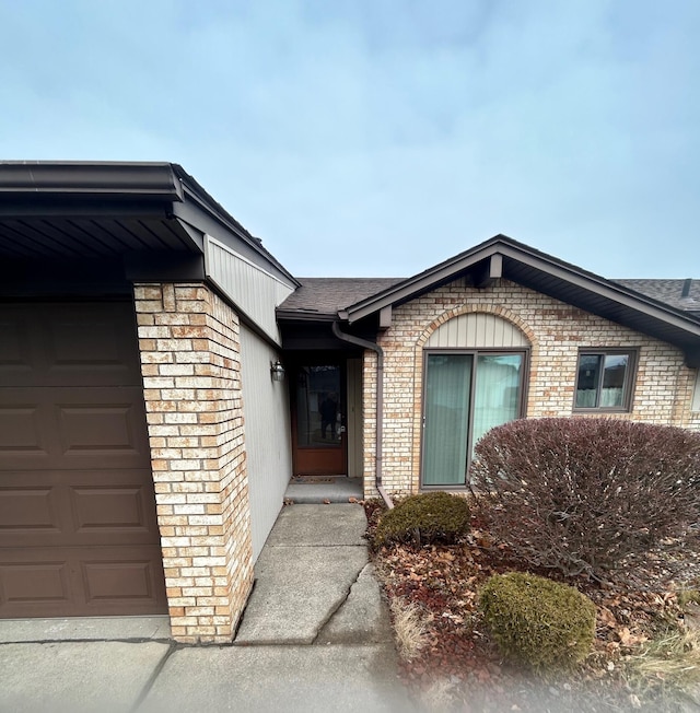 property entrance featuring an attached garage, a shingled roof, and brick siding