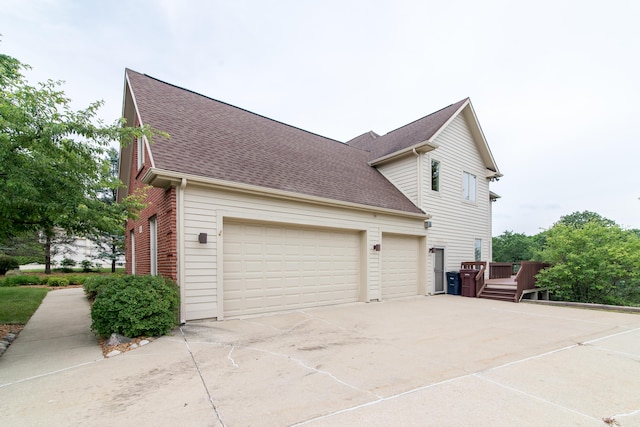 view of side of property featuring an attached garage, a shingled roof, concrete driveway, and brick siding