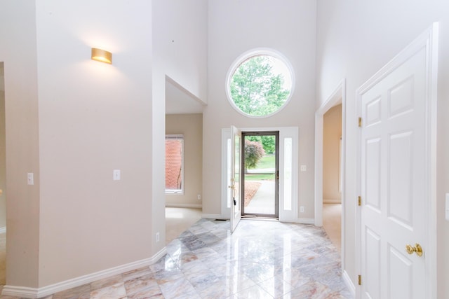 foyer featuring marble finish floor, a high ceiling, and baseboards