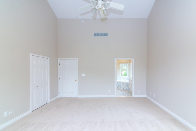 spare room featuring light carpet, baseboards, visible vents, a ceiling fan, and a towering ceiling