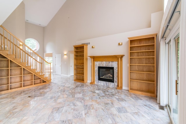 unfurnished living room with high vaulted ceiling, a high end fireplace, visible vents, and stairs