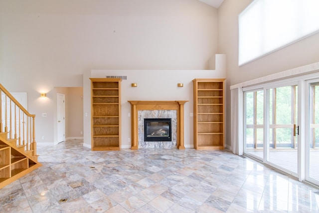 unfurnished living room with a high ceiling, a premium fireplace, visible vents, baseboards, and stairs