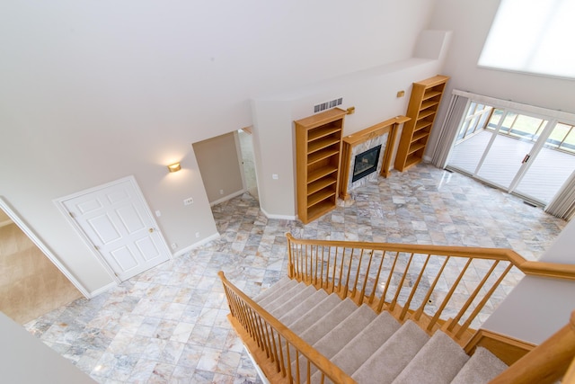 stairs featuring baseboards, visible vents, a towering ceiling, and a tiled fireplace