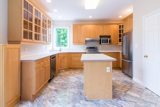 kitchen with light brown cabinets, stainless steel appliances, light countertops, a center island, and glass insert cabinets