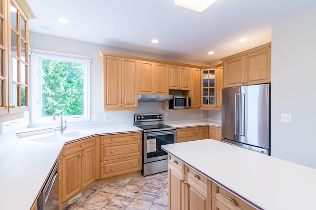 kitchen with light brown cabinets, under cabinet range hood, stainless steel appliances, a sink, and light countertops